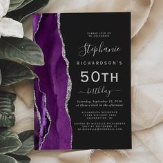 a black and purple 50th birthday party card with silver foil on the edge, surrounded by greenery