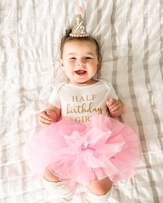 a baby wearing a pink tutu and a tiara laying on a white sheet