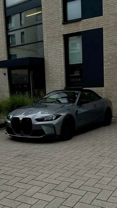 a grey sports car parked in front of a building on a brick sidewalk next to a parking meter