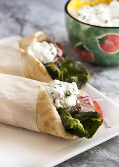 two pita sandwiches on a white plate next to a bowl of yogurt