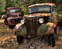 an old rusted truck sitting in the middle of a field next to another rusty car