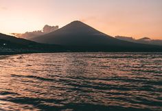 the sun is setting behind a mountain in the ocean