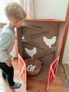 a little boy standing in front of a cardboard chicken coop