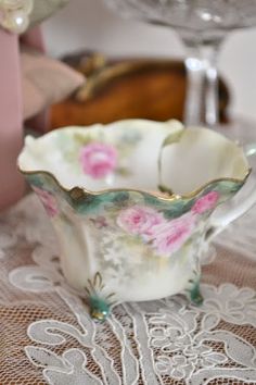 there is a small cup that has pink flowers on it and sits on a lace tablecloth