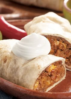 two burritos on a plate with sour cream in the middle and salsa around them