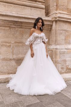 a woman in a white wedding dress standing on the sidewalk