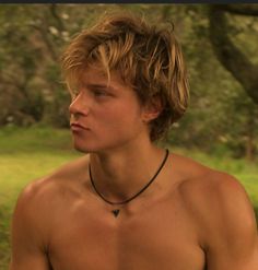 a shirtless young man with no shirt on sitting in the grass and looking off into the distance