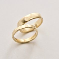 two gold wedding rings sitting on top of a white surface with one ring in the middle