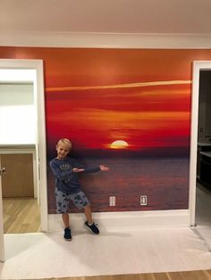 a young boy standing in front of a wall with a painting on it's side