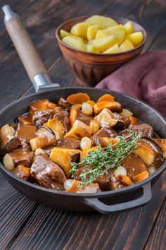 a skillet filled with meat and potatoes on top of a wooden table