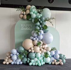 a birthday cake with balloons and greenery on the top is decorated in pastel colors