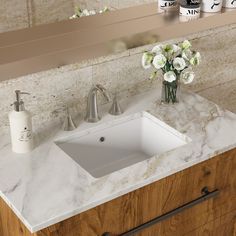 a bathroom sink sitting under a mirror next to a vase with flowers on top of it