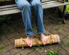 a woman sitting on top of a wooden bench next to a bamboo mat with her feet propped up