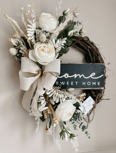 a wreath with white flowers and greenery hangs on the wall next to a sign that says home sweethome