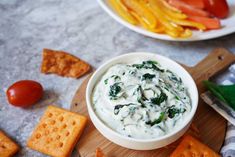 a bowl of dip surrounded by crackers and vegetables