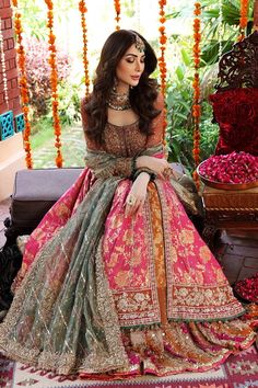 a woman in a pink and green lehenga sitting on a couch with flowers