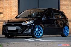 a small black car with blue rims parked in front of a bricked building