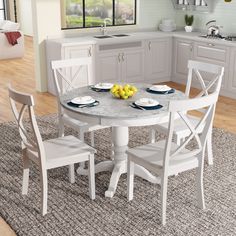 a white kitchen table with four chairs and a bowl of fruit on the dining room table