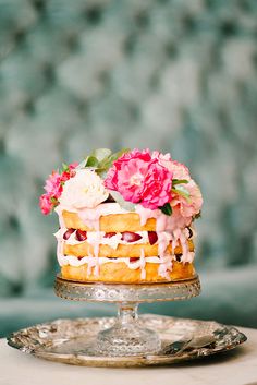 a cake with frosting and pink flowers on top sitting on a silver platter