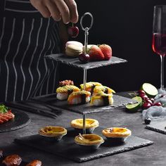 a person is serving food on three trays with wine glasses and utensils