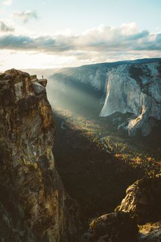 a person standing on the edge of a cliff looking down at trees and mountains in the distance