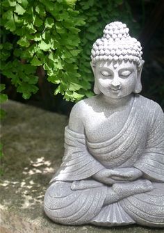 a buddha statue sitting on top of a stone slab next to a tree and bushes