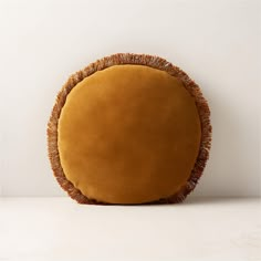 an orange round cushion with fringes on the bottom and sides sitting on a white surface