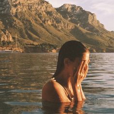 a woman is floating in the water with her hands to her face and looking off into the distance