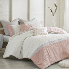 a white bed with pink and grey comforters in a room next to a window