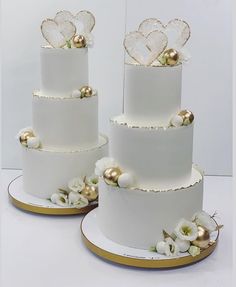 three tiered white wedding cake with gold decorations and flowers on each layer, sitting next to each other