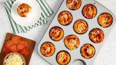 a muffin tin filled with mini pizzas on top of a counter next to a bowl of cheese