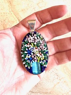 a hand holding a blue glass pendant with flowers on it's side and an oval shape