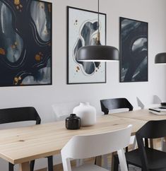 a dining room table with chairs and pictures on the wall above it, along with two black lamps