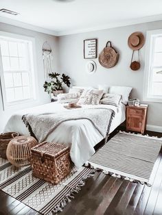 a bedroom with white bedding and baskets on the wall, rugs in front of window