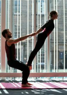 a man and woman are doing yoga in front of large windows with their hands together