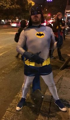 a man dressed as batman standing on the side of a street at night with his hands in his pockets