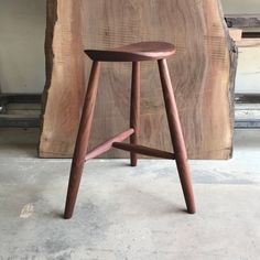 a wooden stool sitting on top of a cement floor next to a piece of wood