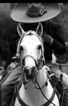 a man riding on the back of a white horse with a hat on his head