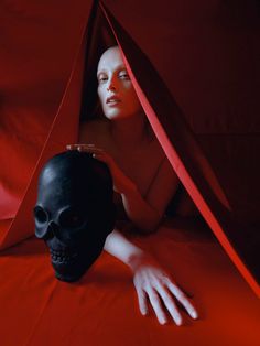 a woman laying on top of a red sheet next to a black skull head in a tent