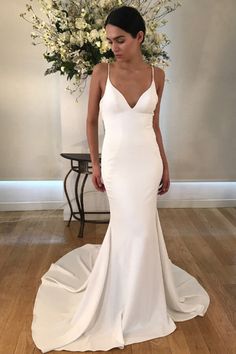 a woman standing in front of a flower arrangement wearing a white dress with spaghetti straps