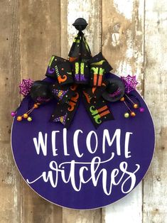 a welcome witches sign hanging on the side of a wooden fence with purple and black decorations