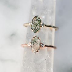 two rings sitting on top of a rock with green and white stones in the middle