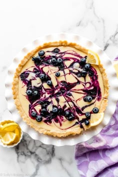 a lemon and blueberry cheesecake on a white plate with a purple towel next to it