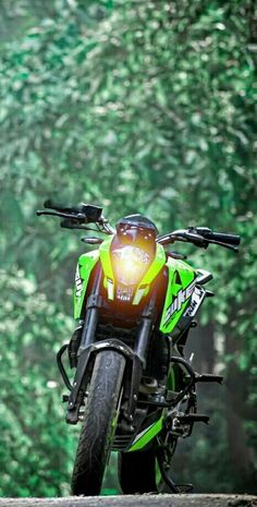 a green and black motorcycle parked on the side of a road in front of trees