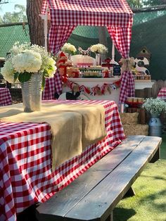 a picnic table set up with red and white checkered cloths on the table