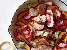 a skillet filled with meat and vegetables on top of a white table next to a spoon