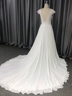 a white wedding dress on display in front of a gray curtained wall with curtains behind it