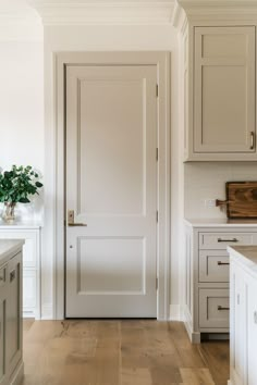 an open door in a white kitchen with wood flooring and cabinets on either side