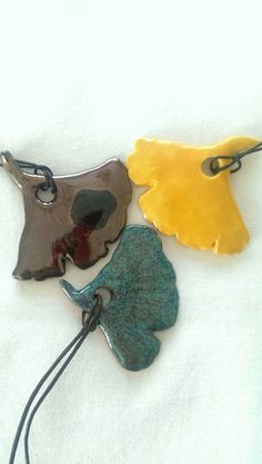 three different colored leaf shaped pendants on a white surface