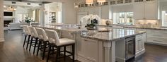 a large kitchen with marble counter tops and white cabinets, along with bar stools